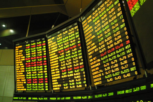 A stock market board shows many different stocks and their figures of three separate screens.