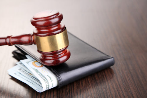 A gavel sits on top of a wallet where money can be seen through the top of it, symbolizing wage stagnation.