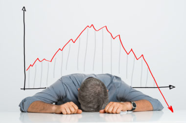 A small business owner lays his head on a table as a graph behind him depicts the financial crisis plunge.