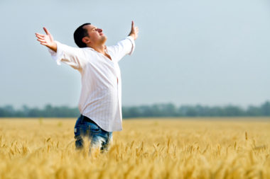 A man rejoicing with his hands up in a field, happy that he doesn't have to pay rent.