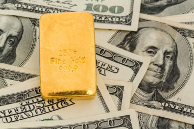 A gold bar sits on top of $100 bills.