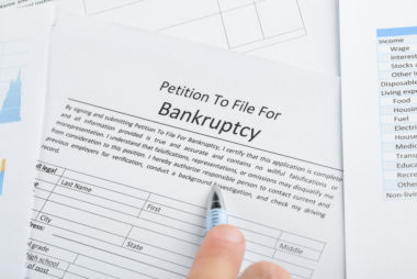 A hand pointing with a pen to a document labeled "petition to file for bankruptcy."