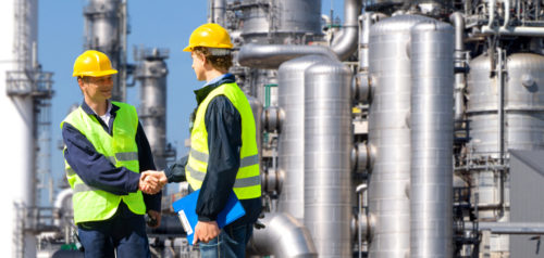 Two chemical engineers shaking hands on a job site.