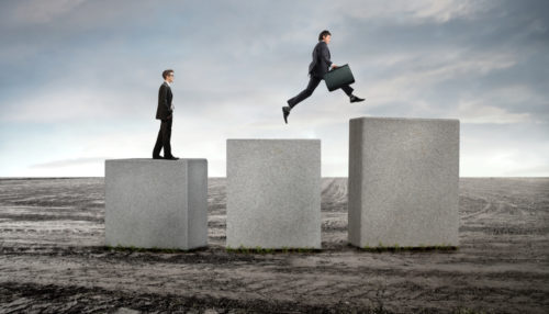 One businessman stands on a stone pillar while another jumps to a higher pillar, signifying career advancement.
