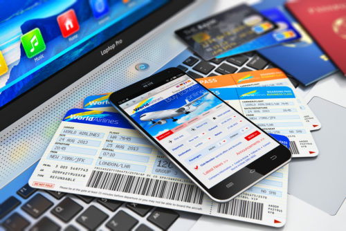 A smartphone with an airline booking site opened up sits on top of plane tickets while sitting next to credit cards and passports.