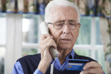 An elderly man reads off his credit card information to a refund scammer.