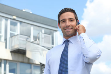 A real estate agent talking on the phone, standing in front of a house.