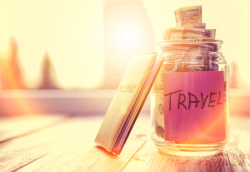 A travel planner leans against a jar that is full of money and labeled "travel."