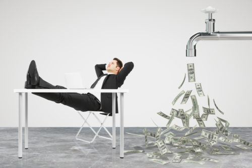 A man in a suit sits back with his feet on a table while a faucet pours out passive income behind him.