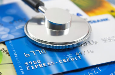 A stethoscope lays on top of a pile of credit cards.