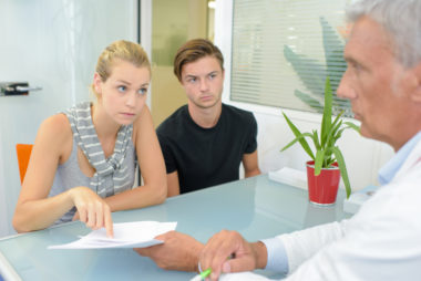 A couple sit across from a doctor at a table, disputing their medical bill.