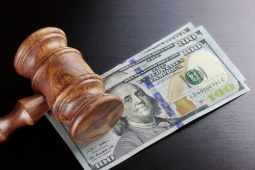 A judges gavel sits on top of $100 bills, signifying a having to pay collateral from not paying a loan.