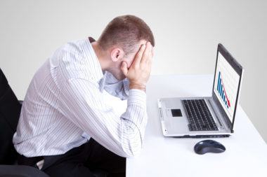 An unhappy man with his head in his arms looking at a bad emotional investment he has made on his laptop.