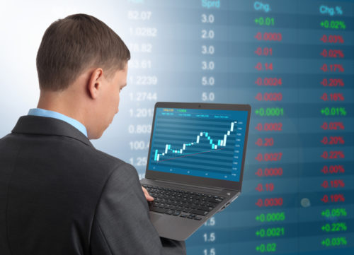 A man checking the market cap of his company on a computer while a graphic of stocks and figures is in the background.