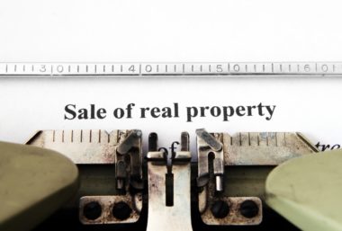 A typewriter has typed out the words "sale of real property" at the top of a piece of paper.