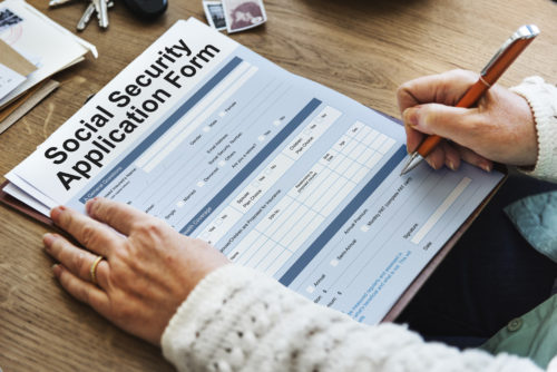 A woman writing on a Social Security application form.