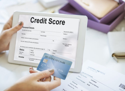 A woman holding a tablet that displays a credit score screen in one hand while holding a rewards card in the other.