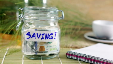 A notebook sits next to a jar of cash marked "saving!"