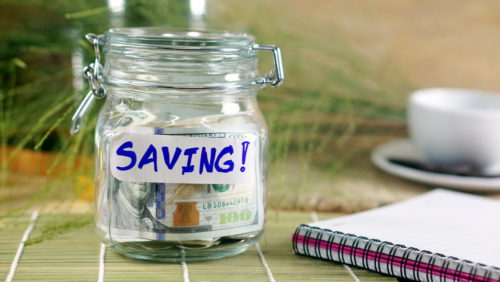 A notebook sits next to a jar of cash marked "saving!"