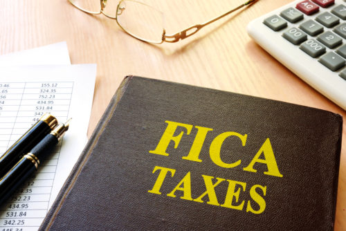 Pens sit on documents and next to a notebook labeled "FICA taxes."