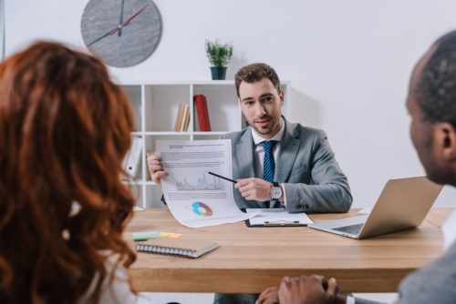 An investment adviser instructing two beginners while pointing at a chart.