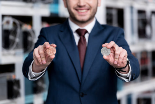 A man holds two bitcoin tokens in front of a cryptocurrency mining farm.