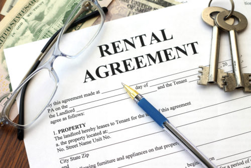 A rental agreement contract sits on top of some cash and under a pen, some keys, and eyeglasses.