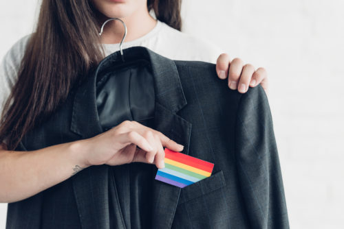 A transgender person pulling a pride flag out of a business suit pocket.
