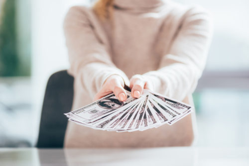 A banker holding fanned out banknotes for a person behind the camera to receive.