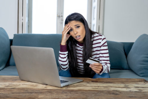 A frustrated woman sitting at a laptop holding a credit card that has had its rewards taxed.