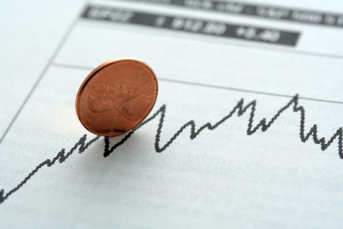 A penny is balanced upright on top of a stock investment graph.