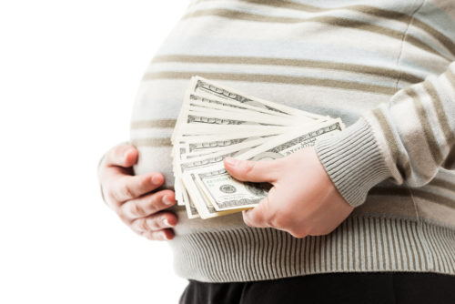 A pregnant, surrogate mother holding her belly in one hand and cash in the other.