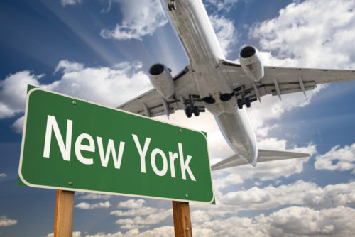 An airplane flies over a road sign that reads "New York."