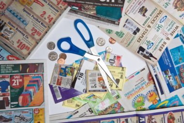 A pair of scissors and coins sit on top of coupons.