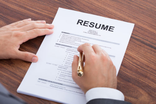 A person pointing to a section of a resume with a pen.