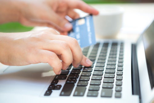 A person types on a laptop while holding a credit card.