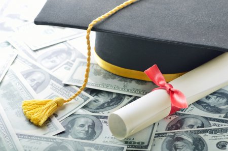 A cap and diploma are laid on top of money.