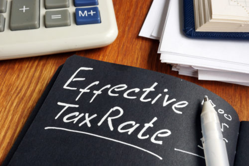 A notebook with black paper sits next to some books and a calculator, with the words "effective tax rate" written on it in white ink.