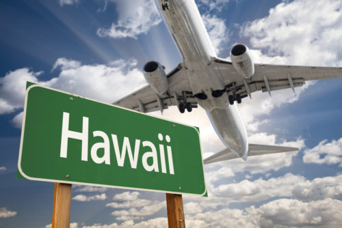 An airplane flies over a road sign that reads "Hawaii."