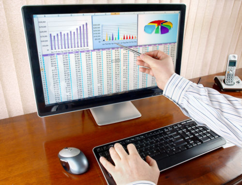A big data engineer points to his computer screen which displays various data and graphs.