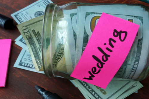 A jar marked "wedding" is filled with various denominations of dollar bills.