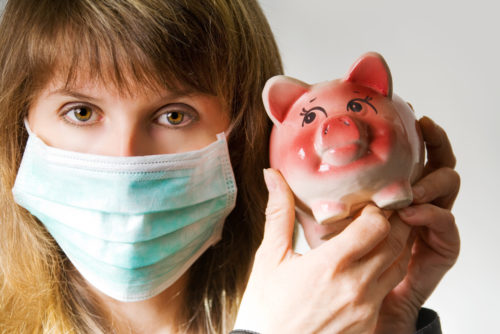 A woman wearing a mask to protect against coronavirus holds a piggy bank next to her.