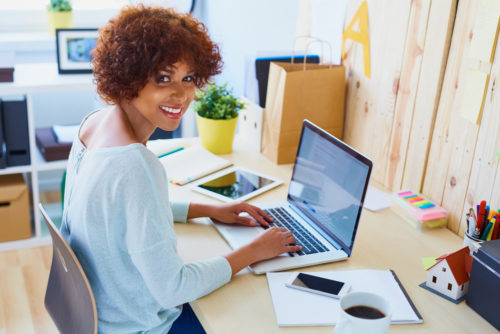 A woman working on her laptop in her home office smiling at the camera.