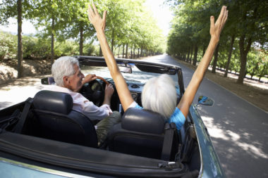 A retired couple driving in a sports car.