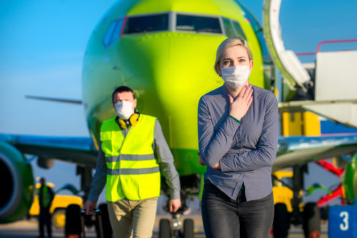 A woman and airport worker wearing medical masks to protect themselves against the coronavirus while walking away from an airplane.