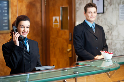 A female receptionist takes a phone call while a male receptionist stands waiting to help customers.