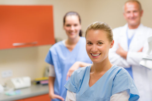 A medical assistant smiles at the camera with her colleagues behind her.
