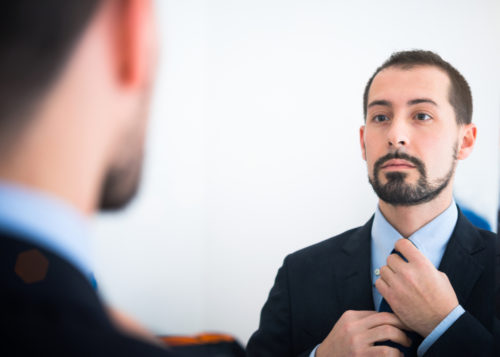 A man fixing his tie in a mirror while preparing for an interview.