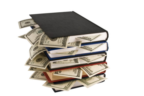College textbooks stacked upon each other with $100 bills sticking out of the books.