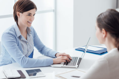 A financial examiner working on her laptop while speaking to a client.